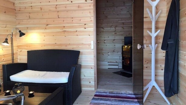 Une pièce chaleureuse aménagée dans un chalet en rondins, avec un lit, une chaise, une petite table, une lampe et un porte-manteau.
