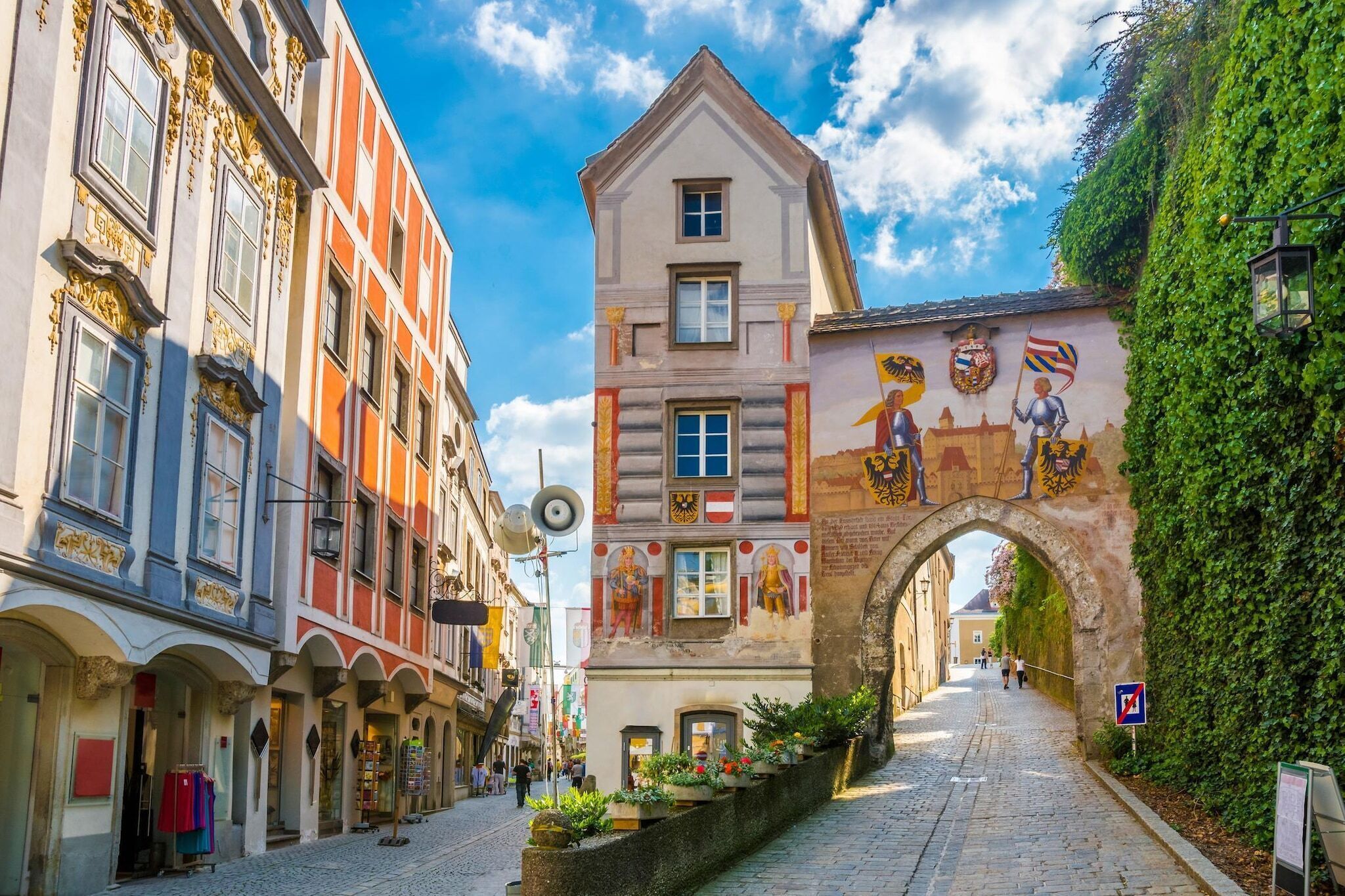 Eine Kopfsteinpflasterstraße mit historischen Gebäuden, einem Bogen und einem Wandgemälde.