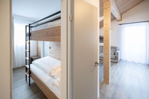 A bunk bed with a ladder, a door leading to another room, and a sofa in a bright room with wooden flooring. - Spacious 8-Person Alpine Apartment with Balcony (Hinterstoder)