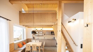 A modern kitchen with wooden cabinetry, a dining area with a bench and chairs, and a staircase leading to an upper level.