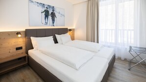A hotel room with a large bed, wooden headboard, and a painting of skiers on the wall.