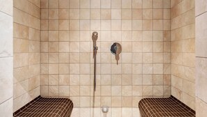 Ducha con azulejos color beige, cabezal de ducha de mano y grifo empotrado.