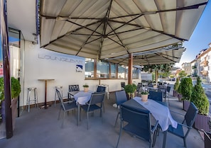 Un área de estar al aire libre con mesas y sillas, un patio cubierto y un cartel que indica LoungeBar.