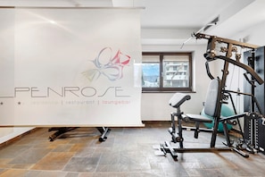 Ein Fitnessraum mit Trainingsgeräten, einem Banner mit dem Schriftzug 'Penrose' und einem Fenster mit Blick auf Gebäude.