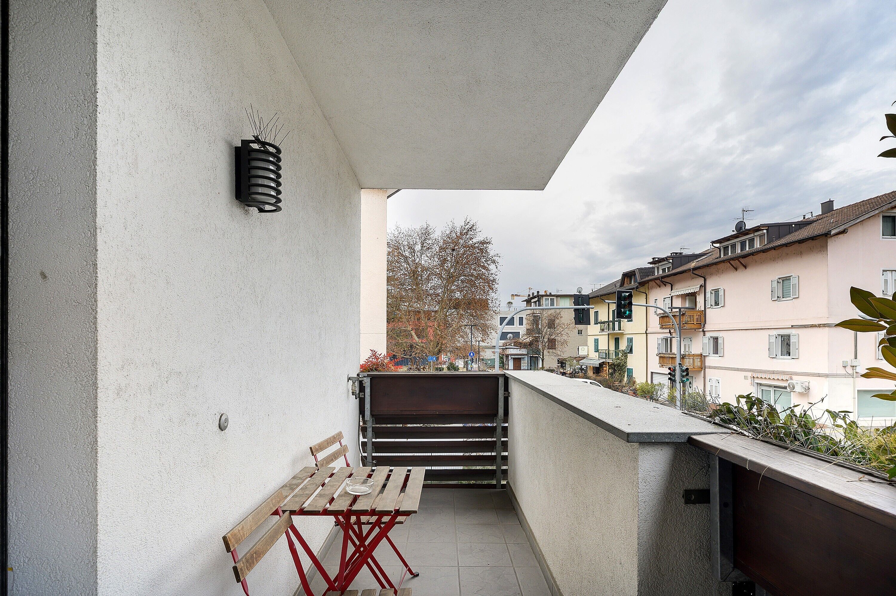 A balcony with a table and bench, a wall-mounted air conditioner, and a view of neighboring buildings.