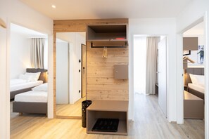 A modern hotel room with a wooden accent wall, a built-in wardrobe, a small seating area, and a kitchenette. - Spacious 3-Bedroom Alpine Apartment for 7 Guests (Hinterstoder)
