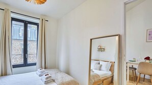 Een hotelkamer met twee bedden, een grote spiegel, een bureau met een stoel en uitzicht op een gebouw door het raam.