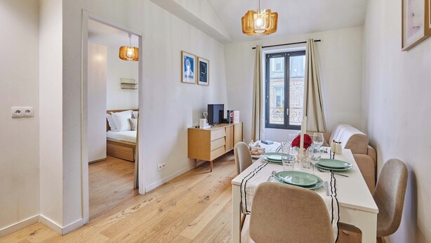 Een moderne eetruimte met een houten tafel gedekt voor twee personen, een televisie op een houten kast en een raam met gordijnen.