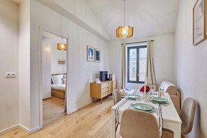 A modern dining area with a wooden table set for two, a television on a wooden cabinet, and a window with curtains. - Charming Apartment Boulogne facing (Boulogne-Billancourt)