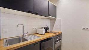 Een keuken met een roestvrijstalen spoelbak, een broodrooster en een koffiezetapparaat op het aanrecht. Boven de spoelbak hangen zwarte kastjes en er zit een vaatwasser onder.