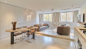 Een moderne woonkamer met een eethoek, grote ramen en een flatscreen televisie.