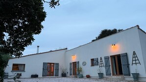 Un bâtiment blanc avec une allée de gravier, des volets en bois et des plantes en pot.