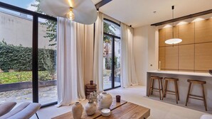 A modern living room with a large window, a wooden table with vases, and a kitchen area with stools. - Architect house Porte Maillot  la Defense Arena (Puteaux)