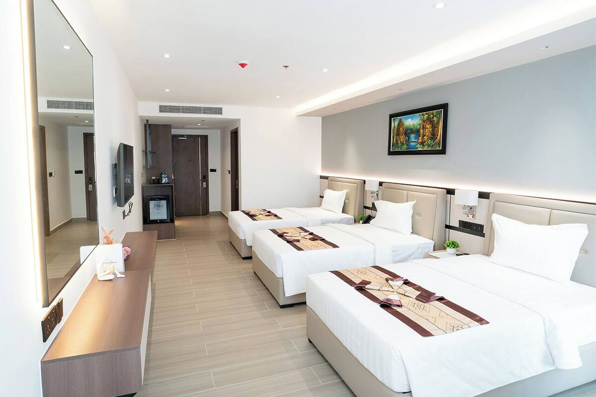 Habitación de hotel con tres camas, un escritorio, un espejo y un cuadro en la pared.
