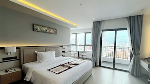 A modern hotel room with a large bed, a bedside table, a nightstand, a desk, and a view of the city through large windows. - LN Hotel & Residence  (Phnom Penh)