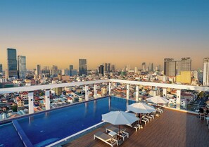 Piscina en la azotea con vistas a la ciudad, sillas de descanso y sombrillas.