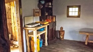 Uma cozinha rústica com fogão a gás, prateleiras de madeira, uma janela e um banco.