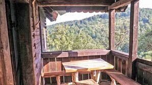 Um deck de madeira com mesa e bancos, com vista para uma encosta arborizada.