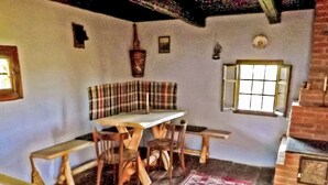 Um interior rústico com uma mesa de madeira e bancos, um banco xadrez, um tapete estampado e uma lareira de tijolos.