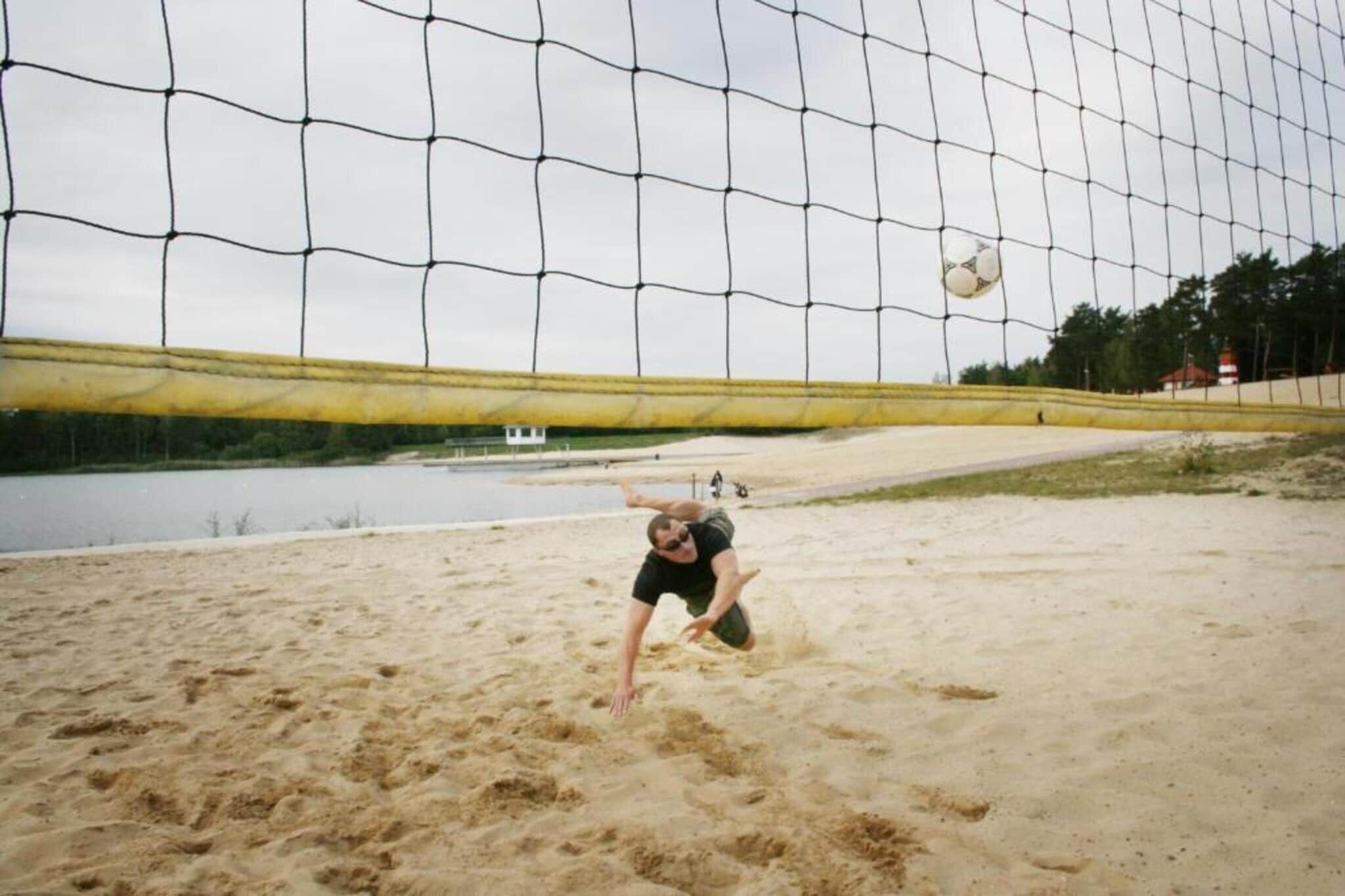 Ein Volleyballnetz mit einem Sandvolleyballfeld und einem Gewässer im Hintergrund.
