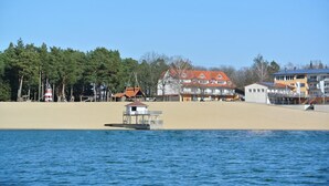 Een kustgebied met een vuurtoren, strandhuizen en een klein bootje op het water.