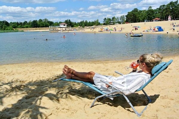 A beach scene with a person relaxing on a beach chair, a sandy beach, and a calm body of water in the background.
