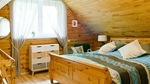 A cozy attic bedroom with a wooden ceiling, a bed with patterned bedding, a nightstand, and a window with sheer curtains. - mit eigenem Parkplatz by Interhome (Ulbroka)