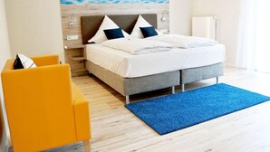 Ein modernes Hotelzimmer mit Bett, einem blauen Teppich, einem gelben Sessel und einem an der Wand befestigten Fernseher.