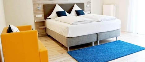 Ett modernt hotellrum med en säng, en blå matta, en gul stol och en tv som är monterad på väggen.