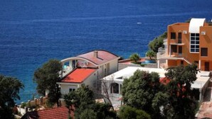 A coastal building with a red roof, multiple balconies, and a view of the sea. - Wohnung mit Pool by Interhome (Bar)