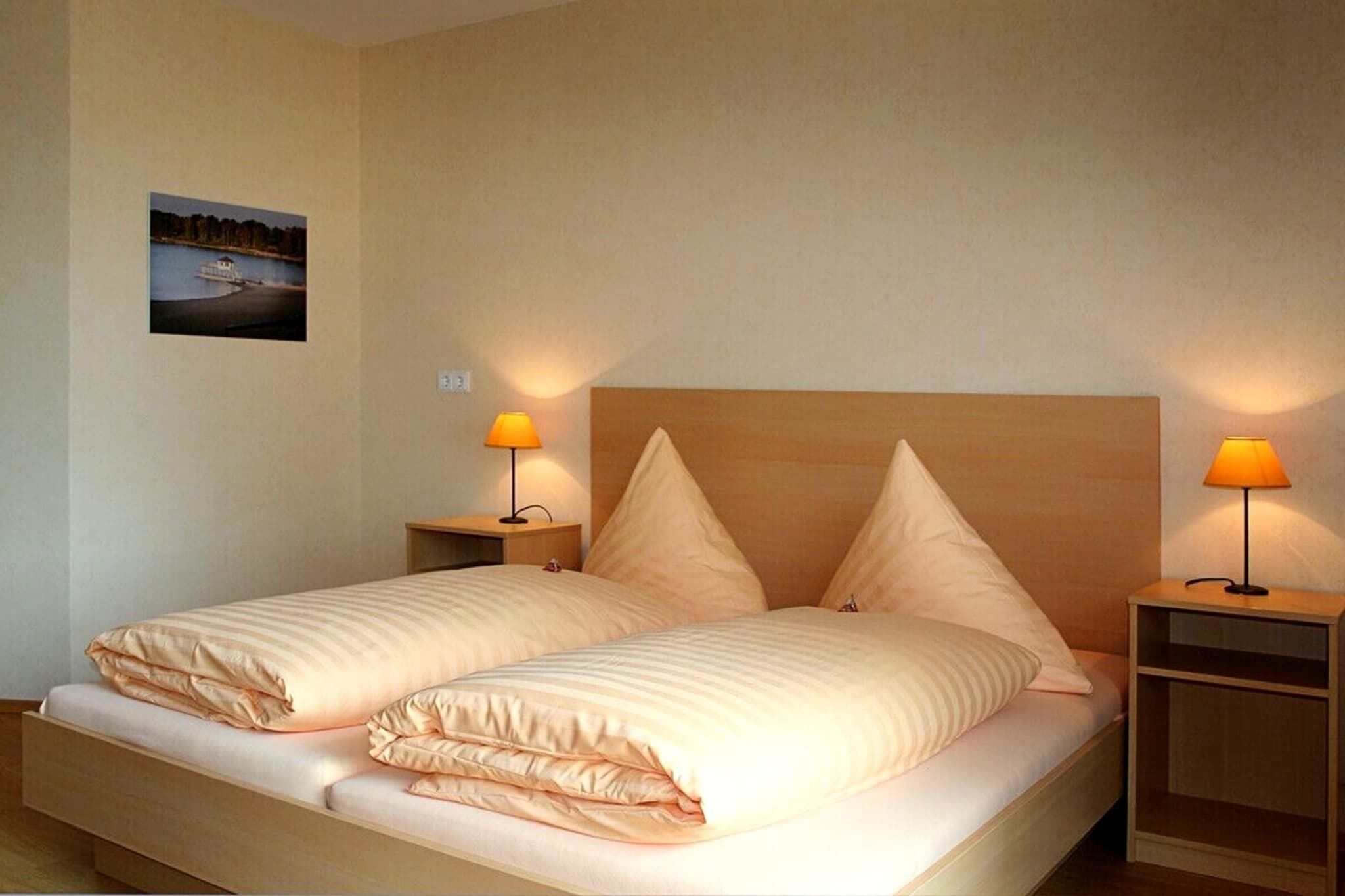 A double bed with two nightstands, each with a lamp, in a room with a wooden headboard and a picture on the wall.
