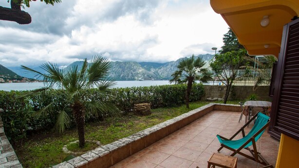 A patio with a view of a lake and mountains, wooden chairs, and a small table. - Familienfreundliche Wohnung direkt am Meer by Interhome (Dobrota)