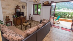 A living room with a sofa, TV, wooden cabinet, and a view of a balcony with a chair. - Familienfreundliche Wohnung direkt am Meer by Interhome (Dobrota)