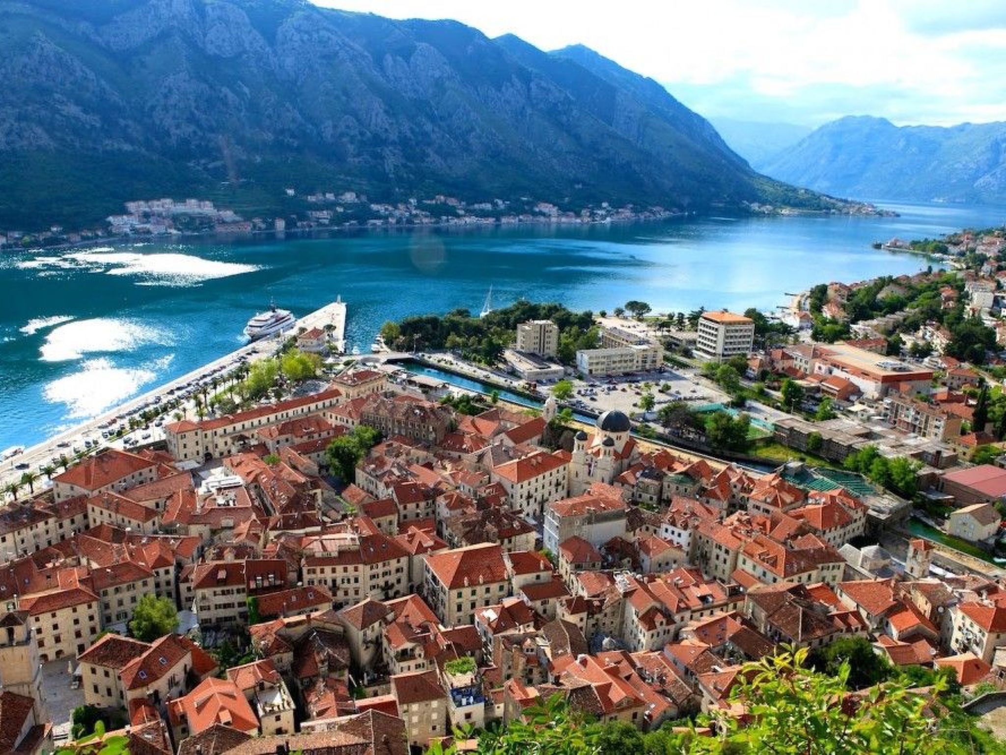 A coastal town with historic buildings, a marina, and a mountainous backdrop.