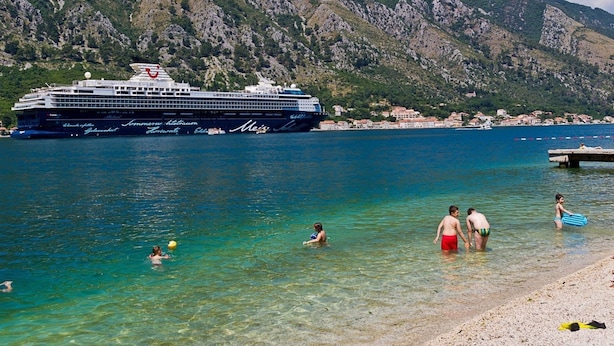Ein Kreuzfahrtschiff liegt im Hafen vor blauem Wasser und felsigen Hügeln.