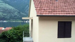 Ein Gebäude mit rotem Ziegeldach, einem Balkon mit Metallgeländern und Blick auf einen See sowie Berge im Hintergrund.