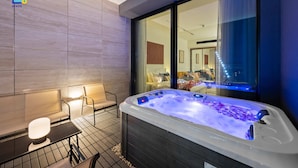 Een moderne badkamer met een bubbelbad, een zithoek en uitzicht op de stad door grote ramen.