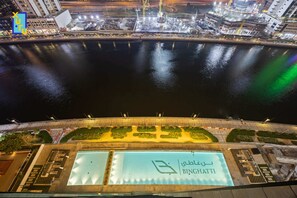 Szenenbild eines Hotels am Wasser bei Nacht, mit einem großen, beleuchteten Poolbereich und einem Schild mit der Aufschrift 'BINGHATTI'.
