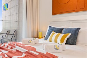 A hotel room with a bed, pillows, and towels with the hotel logo. There is a chair and a table outside the window. - The Velvet Apex Studio w/ Jacuzzi Trillionaire (Dubai)