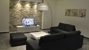 Een moderne woonkamer met een stenen accentmuur, een flatscreen-televisie, een witte console, een zwarte bank en een vloerlamp.
