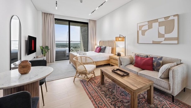 Quarto de hotel moderno com cama, sofá, mesa de jantar e varanda com vista.