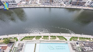 Vista aérea de um imóvel à beira-mar com piscina, áreas ajardinadas e um edifício grande com placas.