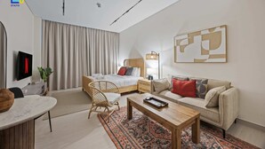 Quarto de hotel moderno com cama, sofá, mesa de centro, televisão e uma grande pintura abstrata na parede.