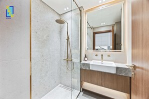 A modern bathroom with a glass-enclosed shower, a marble countertop sink, and wooden cabinetry. - Timeless & Textured Studio w/ Jacuzzi Trillionaire (Dubai)