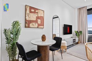 A modern hotel room with a round dining table, black chairs, a large abstract painting, a flat-screen TV with Netflix logo, and a large window with curtains. - Timeless & Textured Studio w/ Jacuzzi Trillionaire (Dubai)