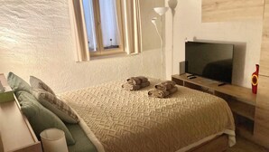 Een slaapkamer met een bed, kussens, een televisie en een lamp.