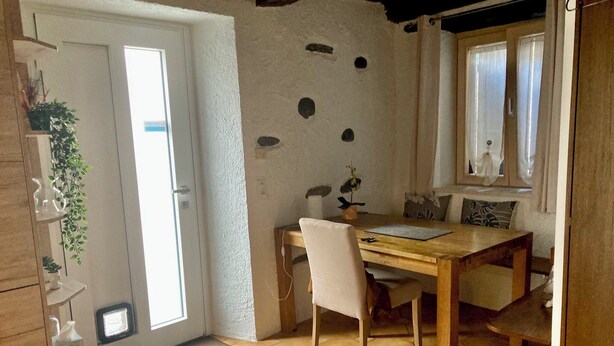 Een kleine keuken met een houten tafel, witte stoelen en een keukeneiland.