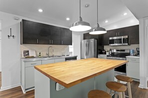 A modern kitchen with dark cabinets, stainless steel appliances, a wooden island, and pendant lighting. - Jasmine Oaks Retreat in beautiful South Tampa (Tampa)