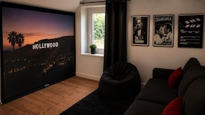 A living room with a large flat-screen TV, a bean bag, a dark sofa, and a window with curtains. - Domaine du Pin – Nature Escape for Groups (15)+ Spa & Activities -South Brittany (LANGUIDIC)