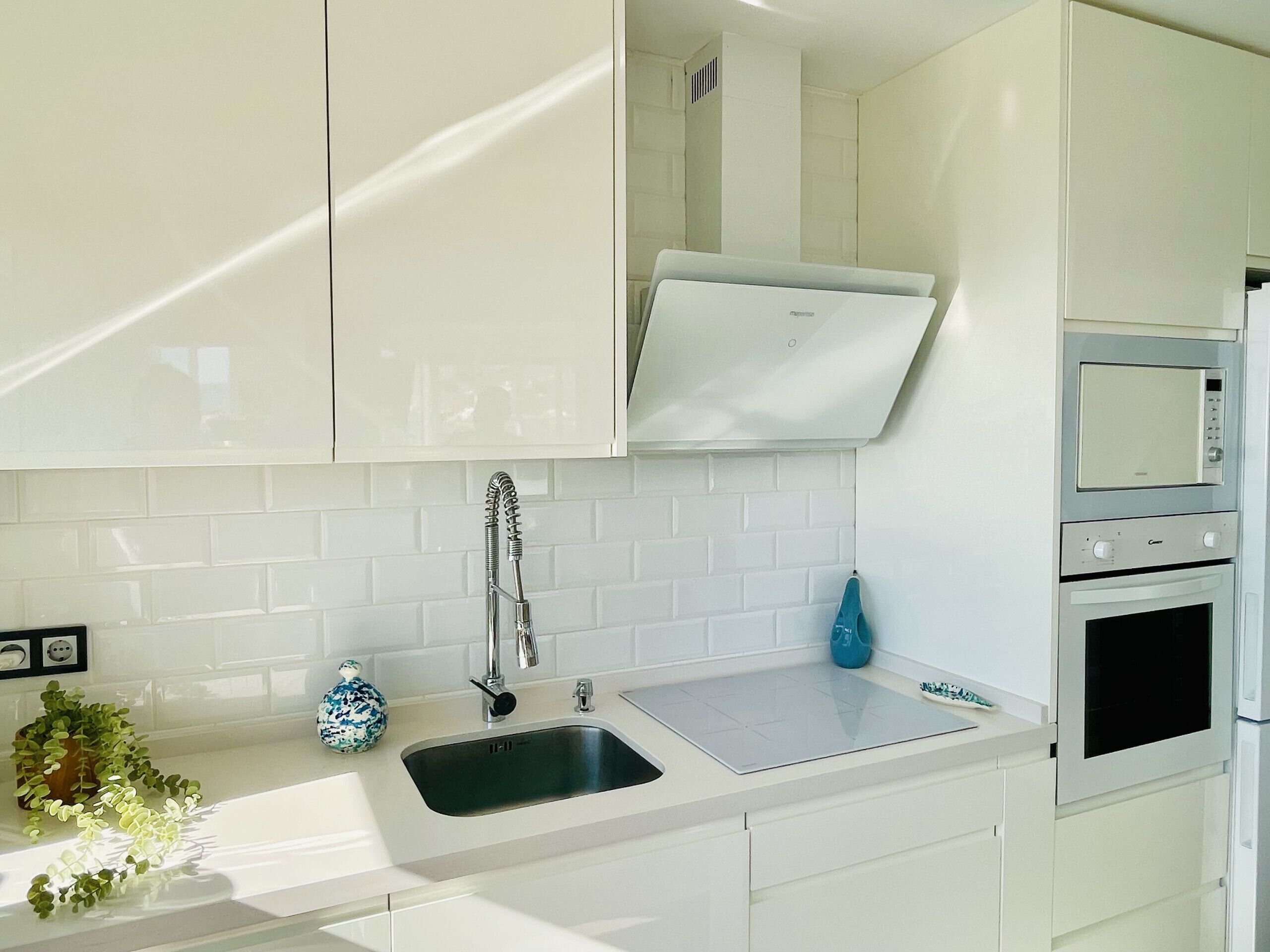A modern kitchen with white cabinetry, a stainless steel sink, a built-in oven, and a microwave.